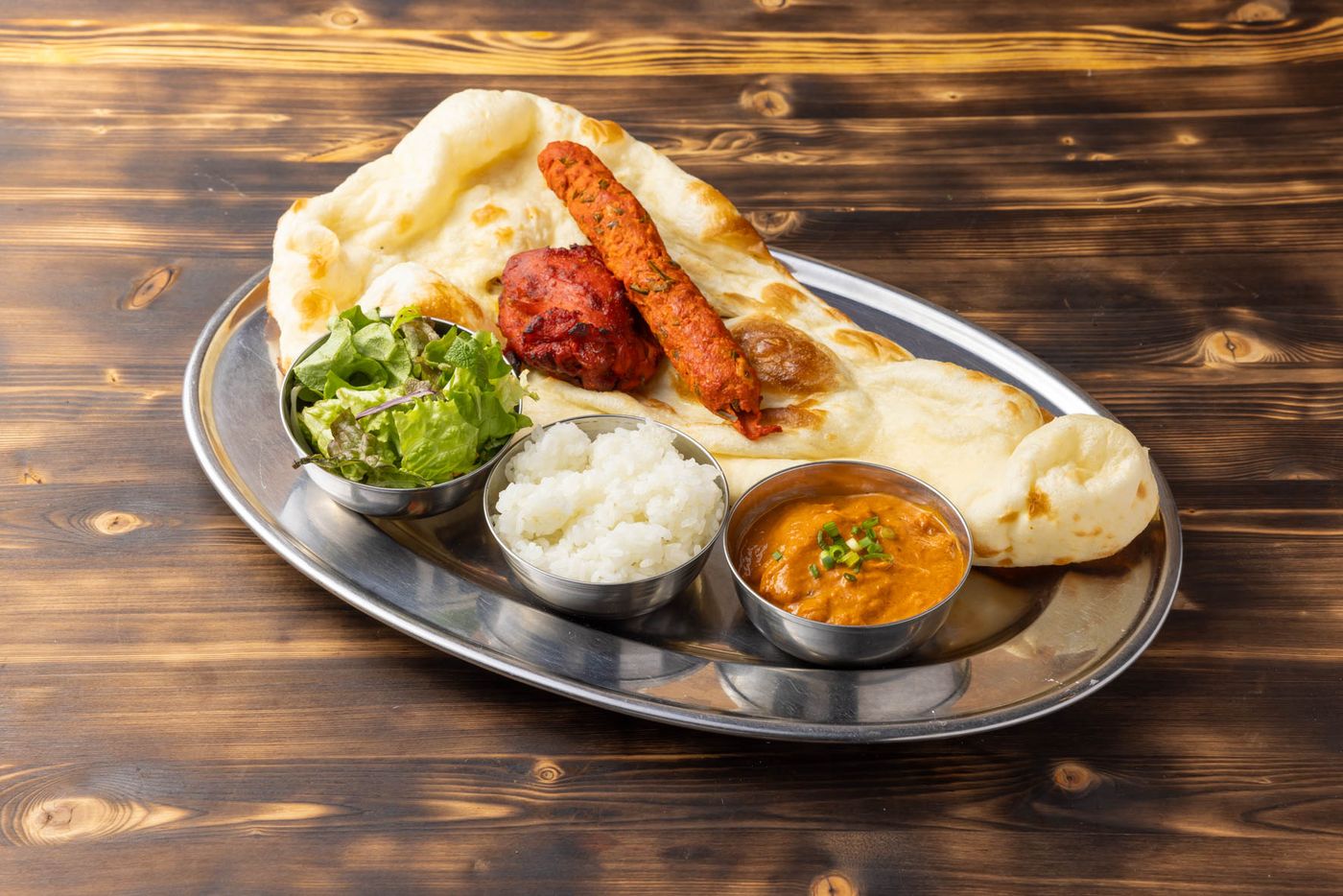 ターリー皿にのった焼きたてナンとタンドリーチキン、スパイスカレーのセット